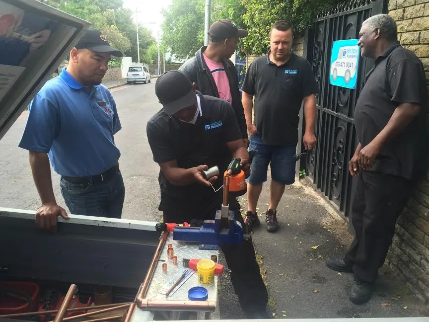 A plumber working at a gate with tools laid out on a board.